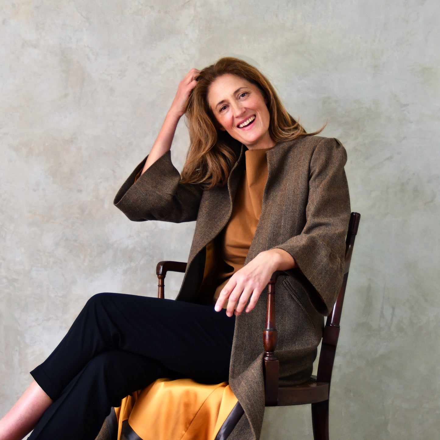 British Made Bell Sleeve A-Line Coat in Brown Cashmere-Mix A Longer length occasion coat in a dark Brown Cashmere mix. This elegant A-Line Coat has bell cuff sleeve and shoulder gather details. Seated View with glimpse of gold silk lining.