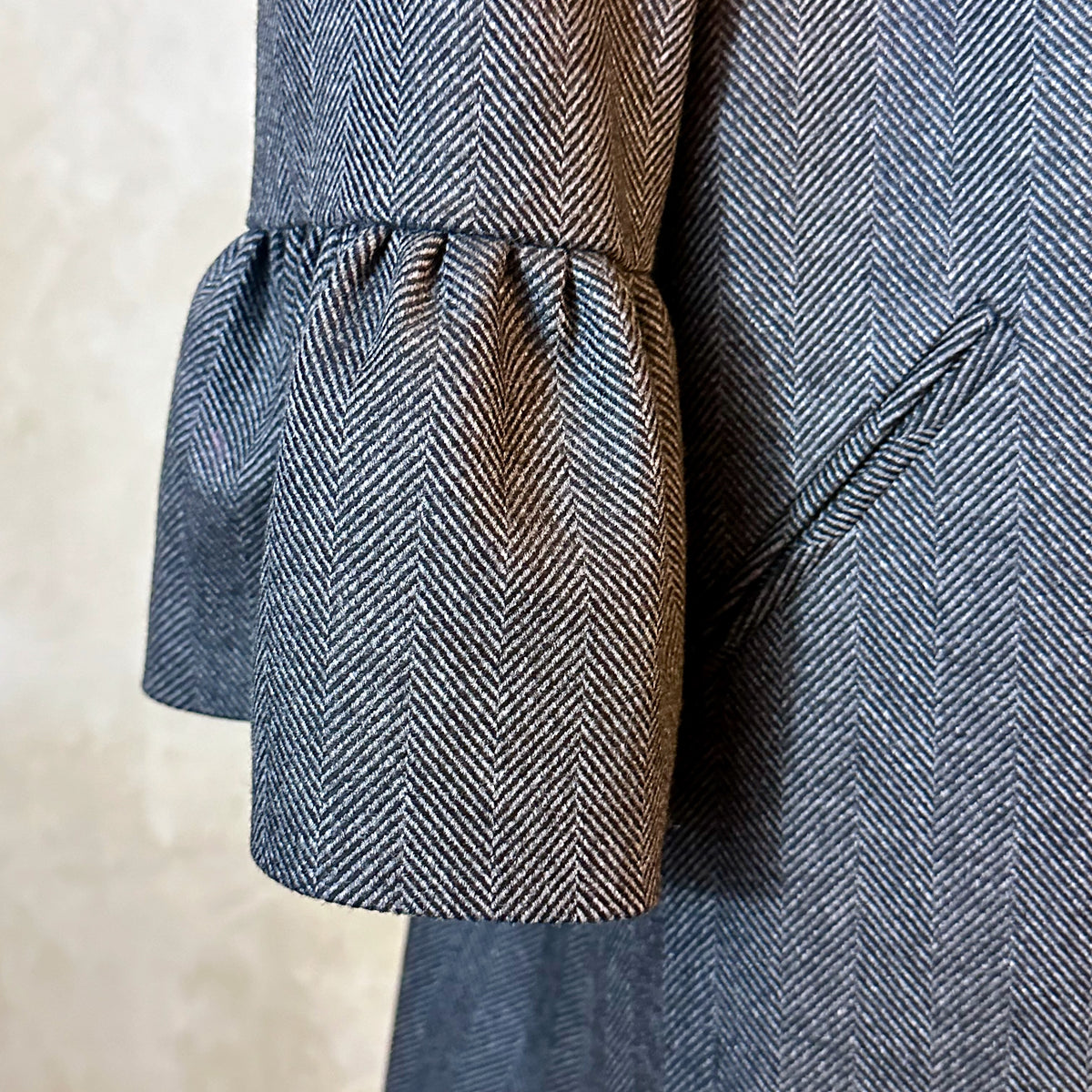 Bell Sleeve A-Line Coat in Charcoal Cashmere Mix Flannel. Bespoke longer length deep grey-coloured A-line coat with gathered shoulder detail, frill cuffs, two slanted pockets to the front and a luscious pink silk lining. Handmade in Britain. Woven in Yorkshire. Cuff and Pocket Detail Shot.