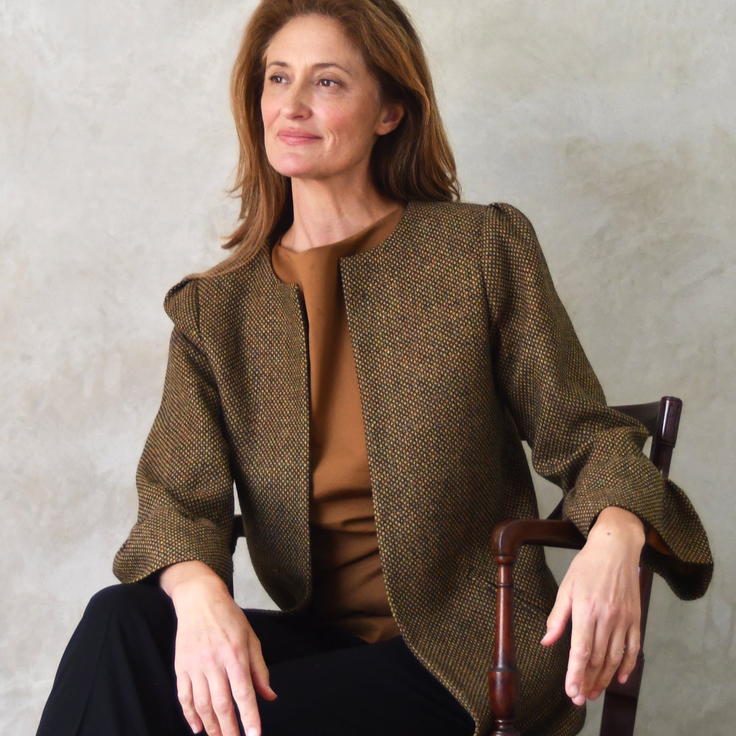 Bell Sleeve A-Line Coat in Green and Orange Patterned Tweed. A longer length A-Line coat in a wonderfully elegant patterned tweed with shoulder and sleeve cuff details. Perfect for winter racing. Seated View.