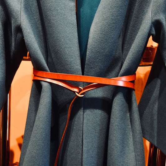 A close-up of a teal coat cinched with the EDNERAT Hazel Double Wrap Belt - 195cm, made from British Saddle Leather with solid brass fittings. Handmade in Britain.
