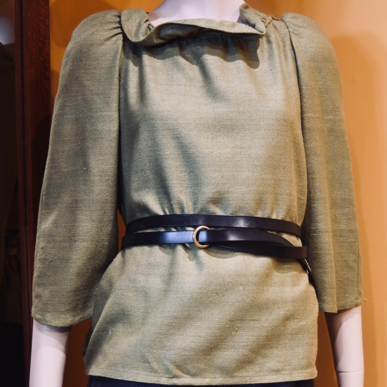 A mannequin wearing a light green, long-sleeved blouse with a gathered neckline is styled with the EDNERAT Black Double Wrap Belt - 200cm, crafted from British saddle leather. Handmade in Britain.