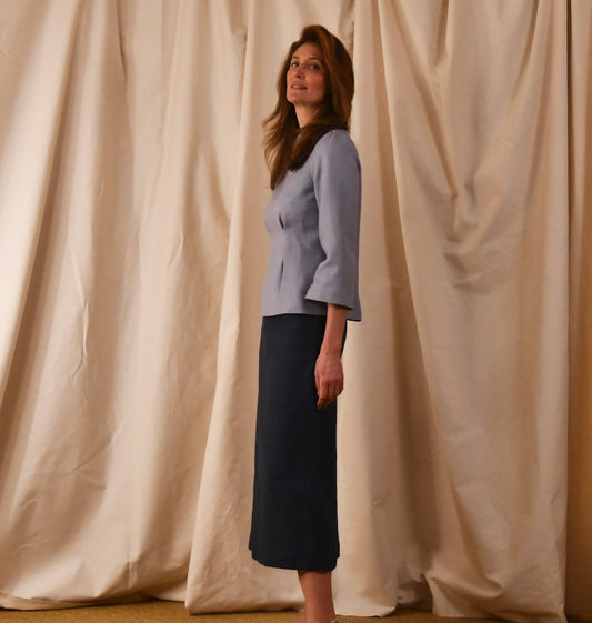 A Bespoke Tailored Boat Neck Blouse in Pale Blue Silk Matka shown with a dark blue linen midi skirt. Handmade in Britain.