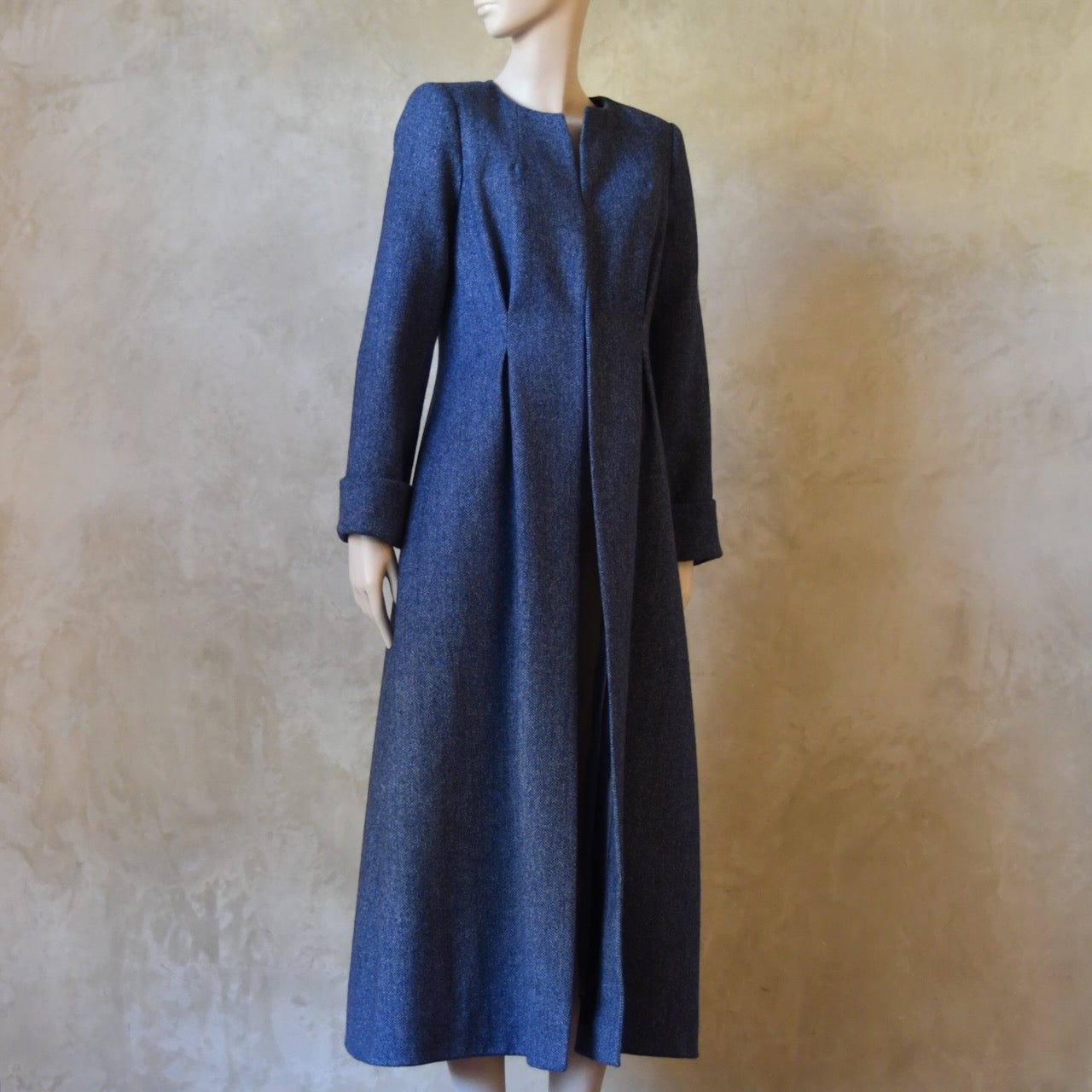 Side view of Bespoke Waisted Tweed Coat, Handmade in London. Denim Blue herringbone tweed dress coat, ideal for winter weddings, race fixtures and other formalwear occasions. Fully lined in pure silk, with optional Nehru collar, fold back cuffs and self-fabric wrap around belt.
Longer or calf length coat.