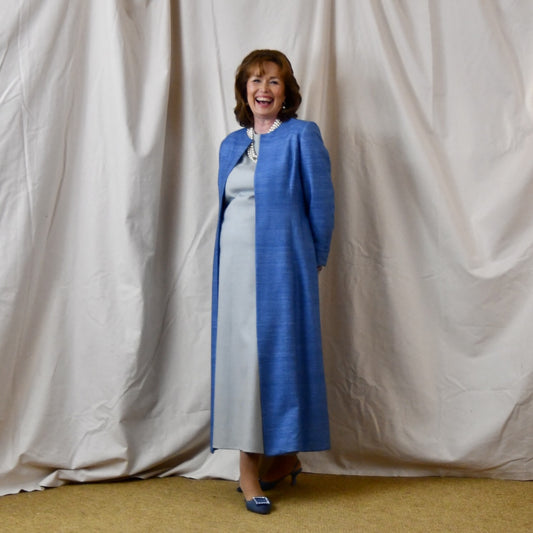 Tailored, Fitted Hourglass shaped coat in a summer-weight Silk Madras in Blue. This is a long-sleeved, calf-length blue summer coat with an hourglass shape. Shown from the side-front. A perfect summer coat for weddings and special occasions. Handmade in Britain.