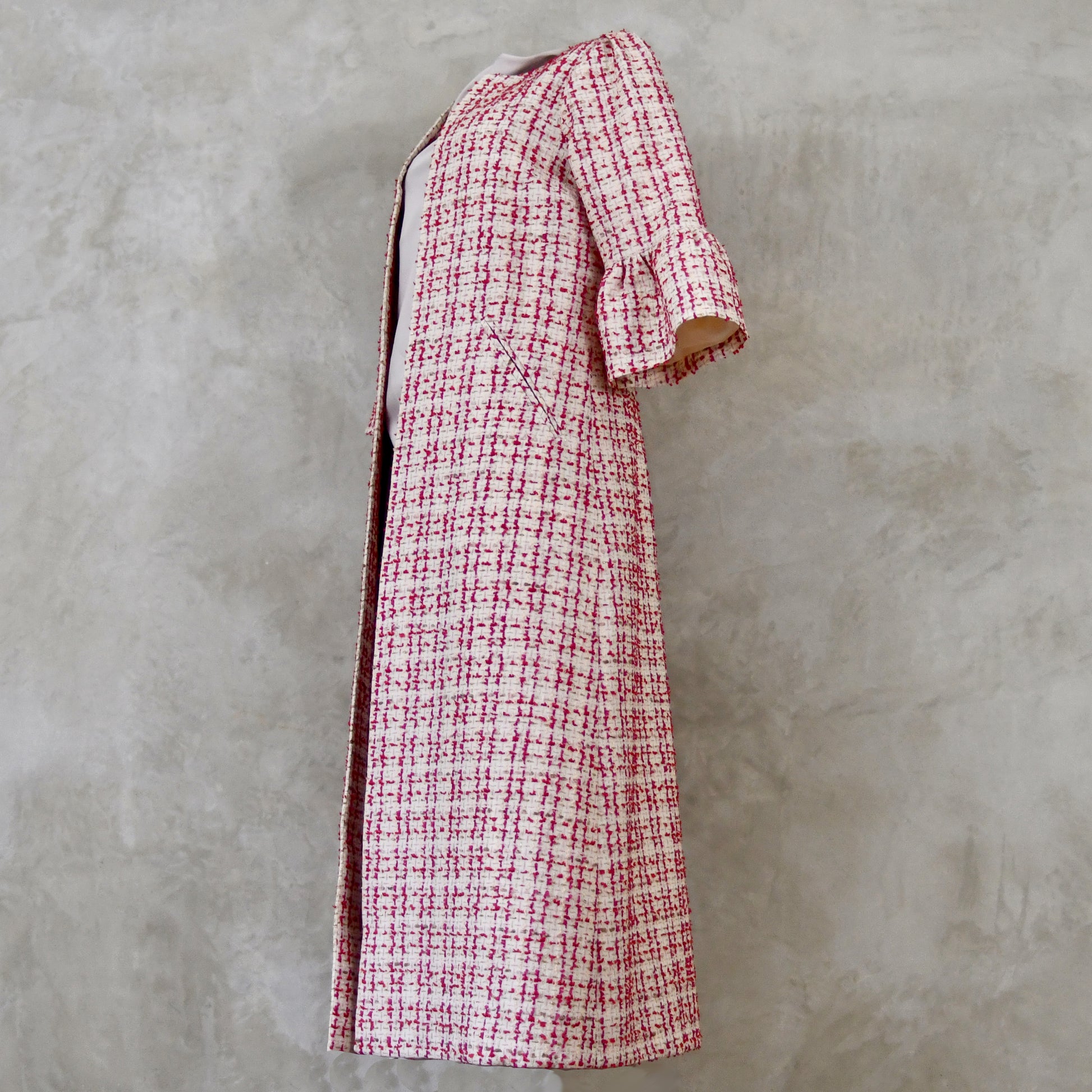 Bell Sleeve A-Line Coat in Pink Patterned Linton Tweeds Boucle. A pretty, longer length A-line coat in a pink, cream and gold check pattern for smart spring and summer occasions. Entirely made in Great Britain. Side View.
