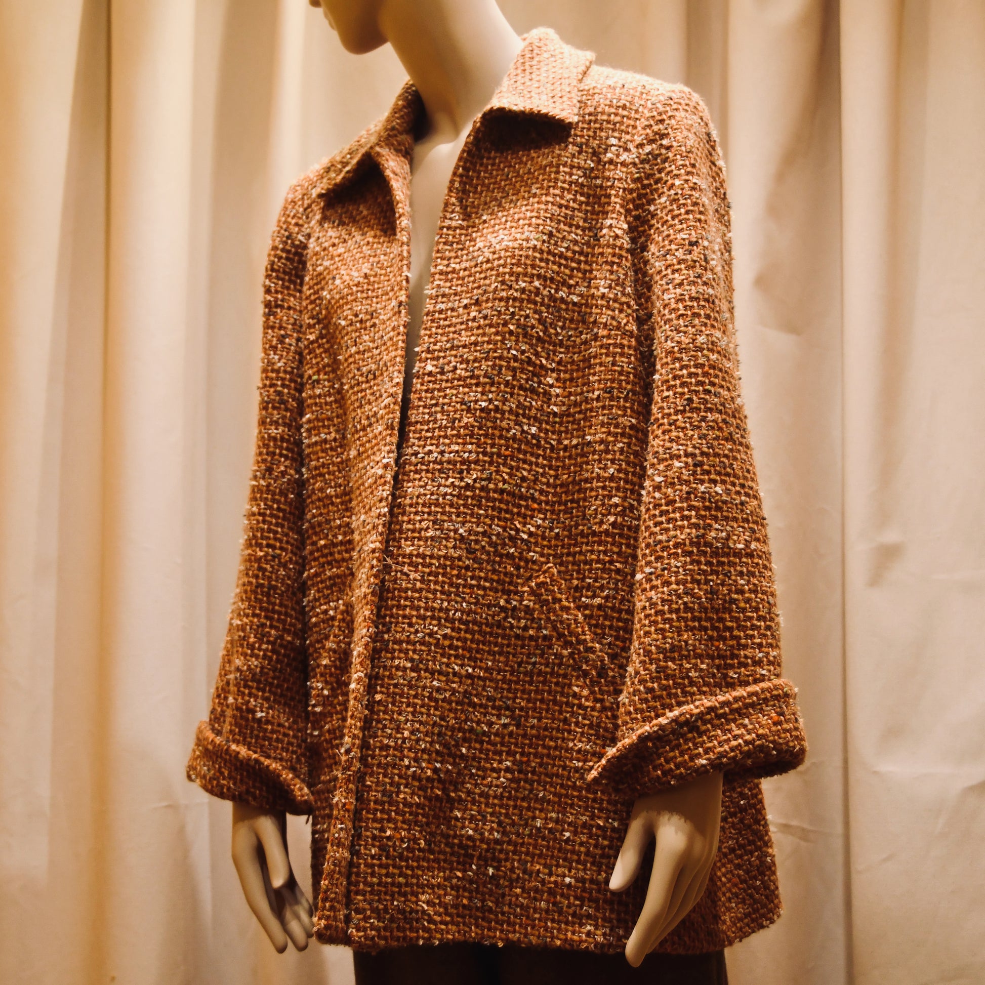 Tailored Swing Jacket in Burnt Orange Wool Mix Bouclé from Linton Tweeds. This bespoke jacket has rolled cuffs and a textured finish and a flared silhouette. Shown from the front and slightly turned to the side. Handmade in Britain.
