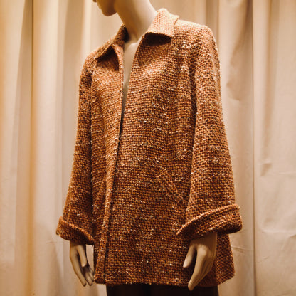 Tailored Swing Jacket in Burnt Orange Wool Mix Bouclé from Linton Tweeds. This bespoke jacket has rolled cuffs and a textured finish and a flared silhouette. Shown from the front and slightly turned to the side. Handmade in Britain.
