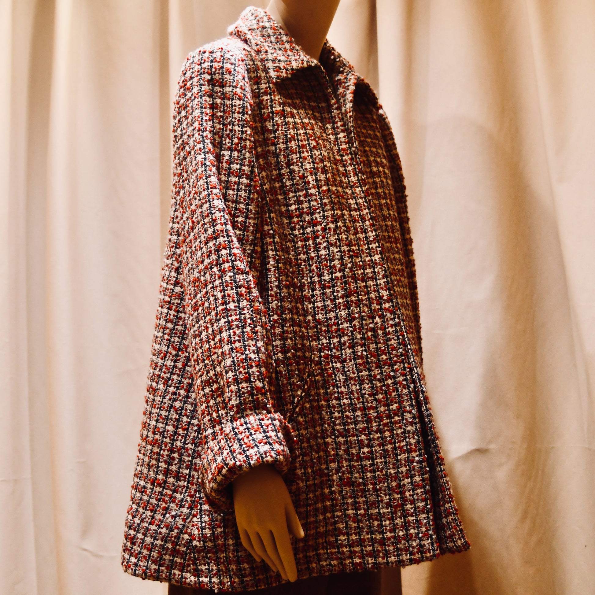 Bespoke Trapeze Swing Jacket in red, ecru, and navy Wool Bouclé from Linton Tweeds. With long sleeves and a collar,  it is shown viewed from the side. Handmade in Britain.