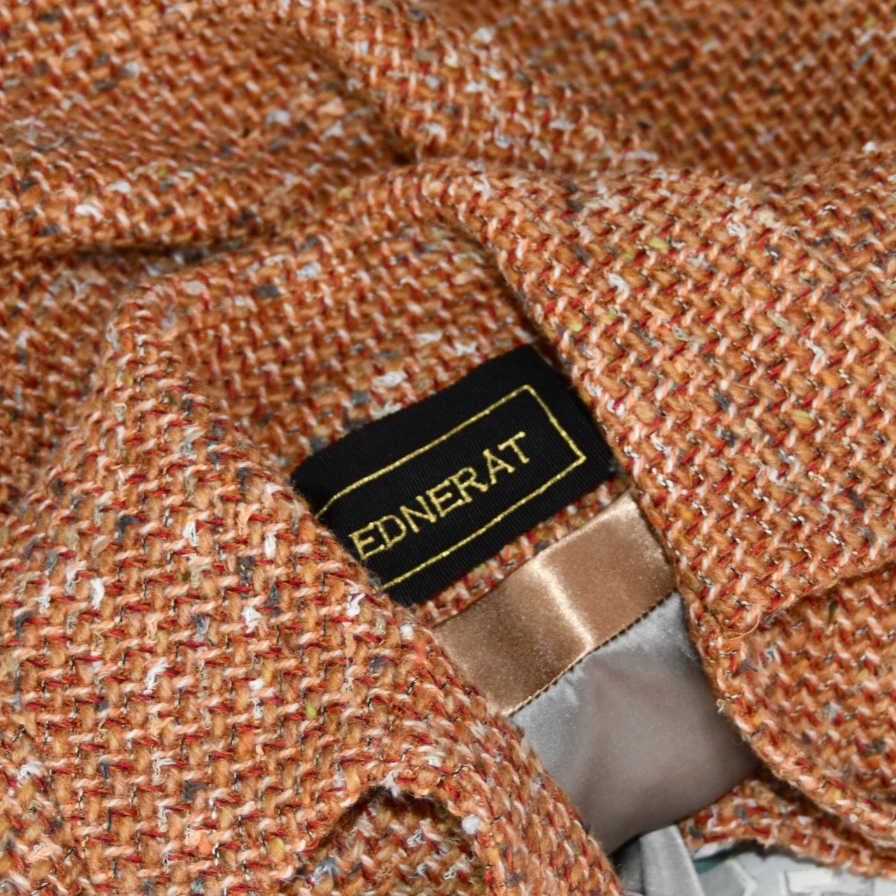 Detailed collar shot of Mid length swing jacket in burnt orange Linton Tweeds wool boucle. Handmade in London, this jacket has fold back cuffs, two slanted pockets to the front and a lift up collar. Easy to wear, it is available in sizes 6 to 20 and bespoke sizing. 
