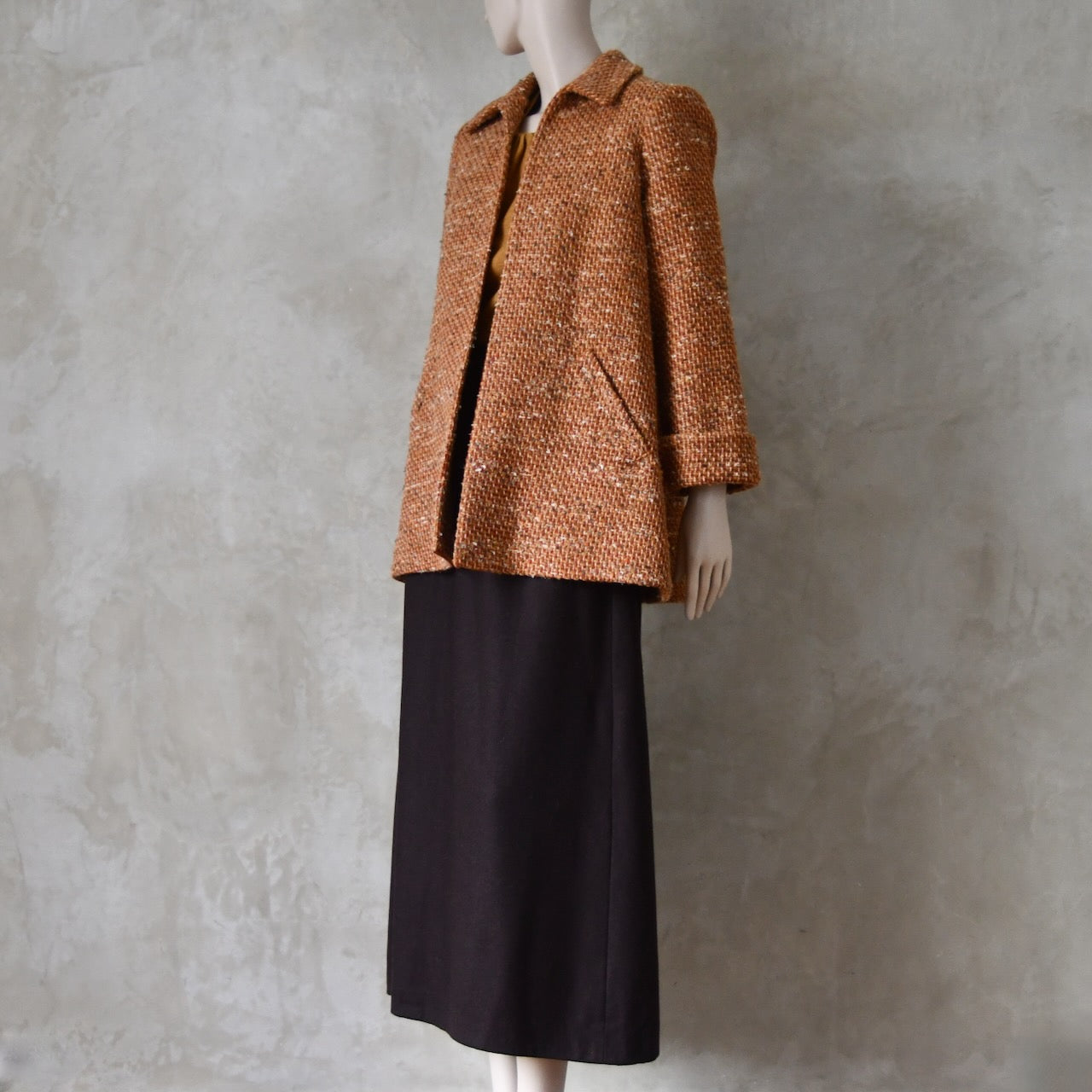 Mid length swing jacket in burnt orange Linton Tweeds wool boucle. Handmade in London, this jacket has fold back cuffs, two slanted pockets to the front and a lift up collar. Easy to wear, it is available in sizes 6 to 20 and bespoke sizing.  Worn over Brown Merino Flannel Skirt.