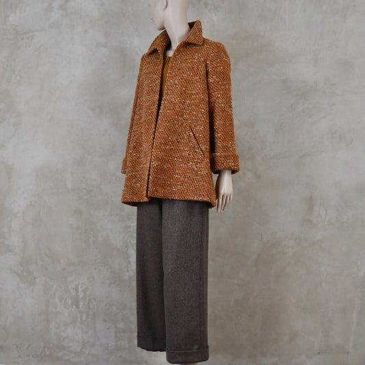 Mid length swing jacket in burnt orange Linton Tweeds wool boucle. Handmade in London, this jacket has fold back cuffs, two slanted pockets to the front and a lift up collar. Easy to wear, it is available in sizes 6 to 20 and bespoke sizing. Worn over Fawn Herringbone Merino Flannel Trousers with turn up.