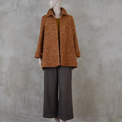 Mid length swing jacket in burnt orange Linton Tweeds wool boucle. Handmade in London, this jacket has fold back cuffs, two slanted pockets to the front and a lift up collar. Easy to wear, it is available in sizes 6 to 20 and bespoke sizing. Worn over Fawn Herringbone Merino Flannel Trousers with turn up.