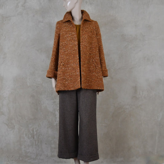 Mid length swing jacket in burnt orange Linton Tweeds wool boucle. Handmade in London, this jacket has fold back cuffs, two slanted pockets to the front and a lift up collar. Easy to wear, it is available in sizes 6 to 20 and bespoke sizing. Worn over Fawn Herringbone Merino Flannel Trousers with turn up.