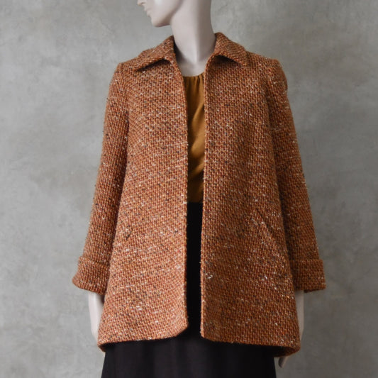 Front open view of Mid length swing jacket in burnt orange Linton Tweeds wool boucle. Handmade in London, this jacket has fold back cuffs, two slanted pockets to the front and a lift up collar. Easy to wear, it is available in sizes 6 to 20 and bespoke sizing. 