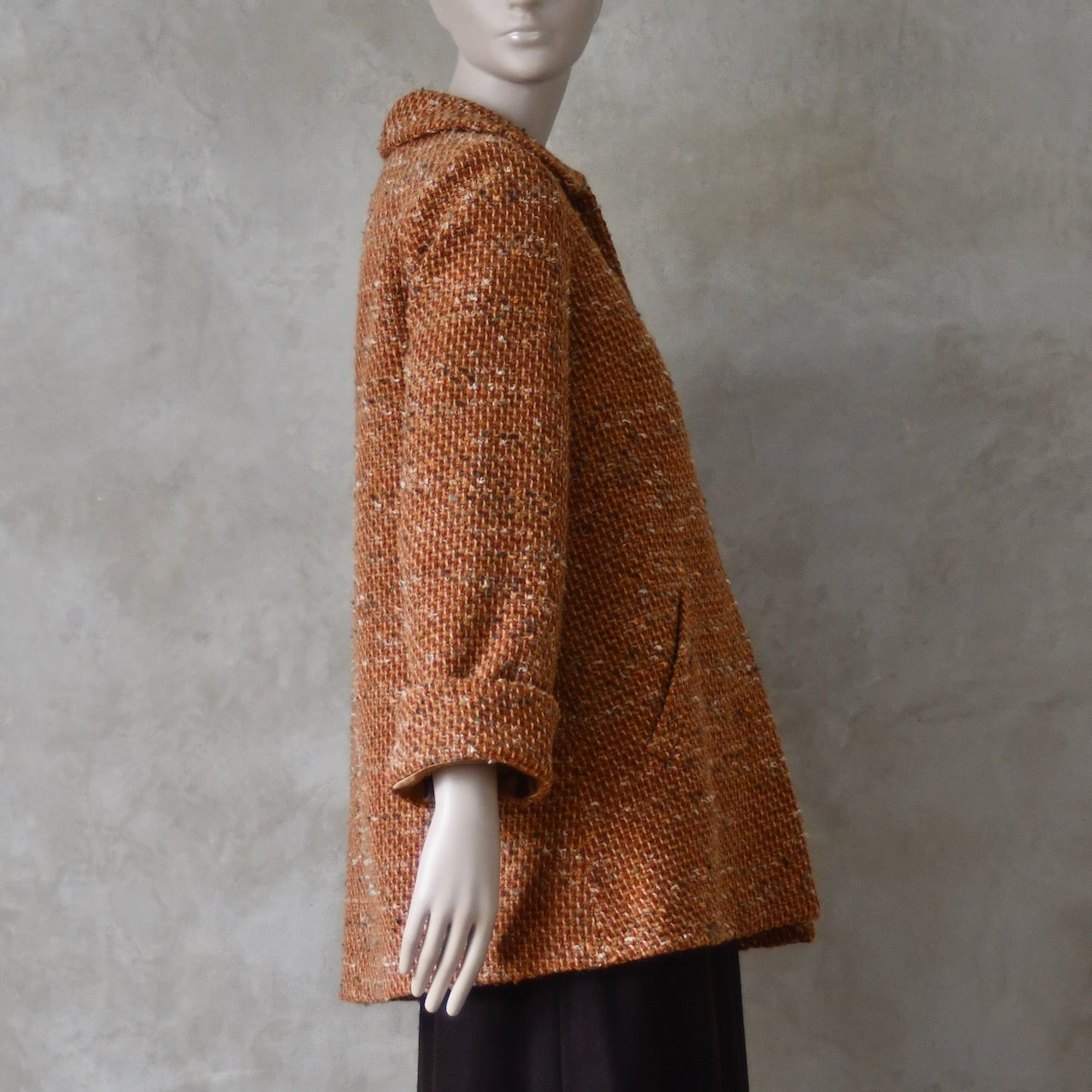 Side view of Mid length swing jacket in burnt orange Linton Tweeds wool boucle. Handmade in London, this jacket has fold back cuffs, two slanted pockets to the front and a lift up collar. Easy to wear, it is available in sizes 6 to 20 and bespoke sizing. 