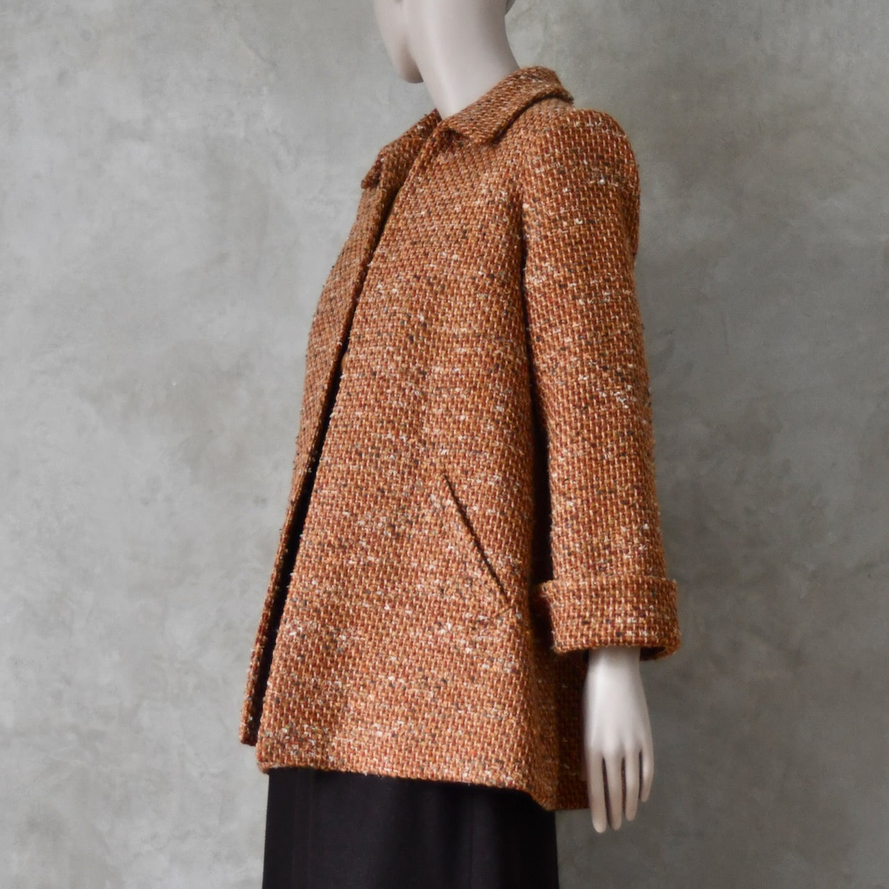 Side on iew of Mid length swing jacket in burnt orange Linton Tweeds wool boucle. Handmade in London, this jacket has fold back cuffs, two slanted pockets to the front and a lift up collar. Easy to wear, it is available in sizes 6 to 20 and bespoke sizing. 