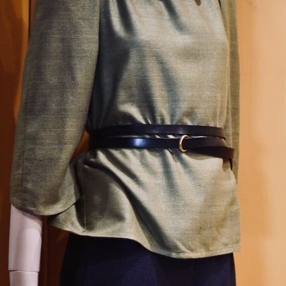 A mannequin wears a loose light olive-green silk blouse with three-quarter sleeves, cinched at the waist by EDNERAT’s Black Double Wrap Belt. Handmade in Britain.