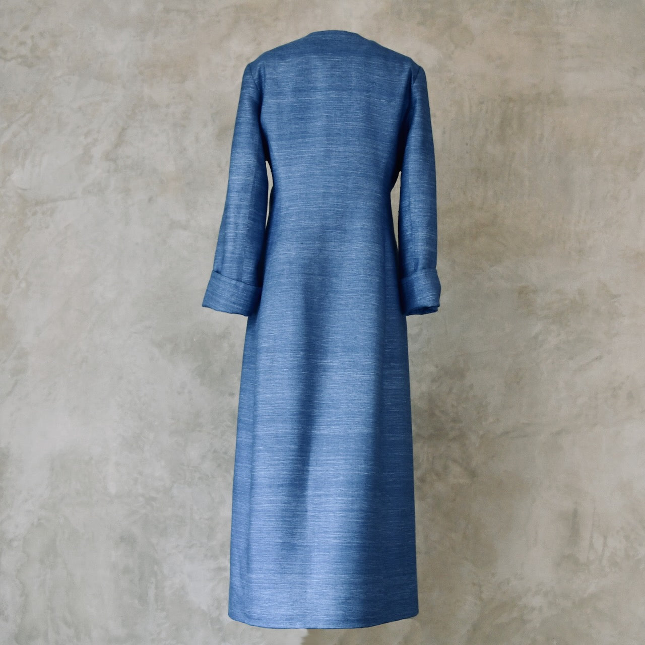 Tailored, Fitted Hourglass shaped coat in a summer-weight Silk Madras in Blue. This is a long-sleeved, calf-length blue summer coat with an hourglass shape. Shown from the back. A perfect summer coat for weddings and special occasions. Handmade in Britain.