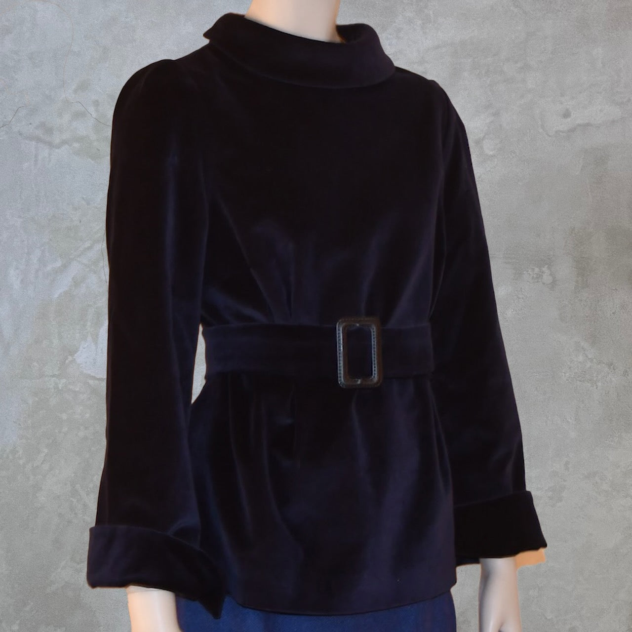 A mannequin showcases EdNerat’s The Tailored Tunic Top Blouse in Velvet, featuring long sleeves, a high collar, and a wide belted waist with a rectangular buckle, ideal for winter evenings against a light textured background.