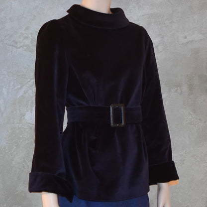 A mannequin showcases EdNerat’s The Tailored Tunic Top Blouse in Velvet, featuring long sleeves, a high collar, and a wide belted waist with a rectangular buckle, ideal for winter evenings against a light textured background.