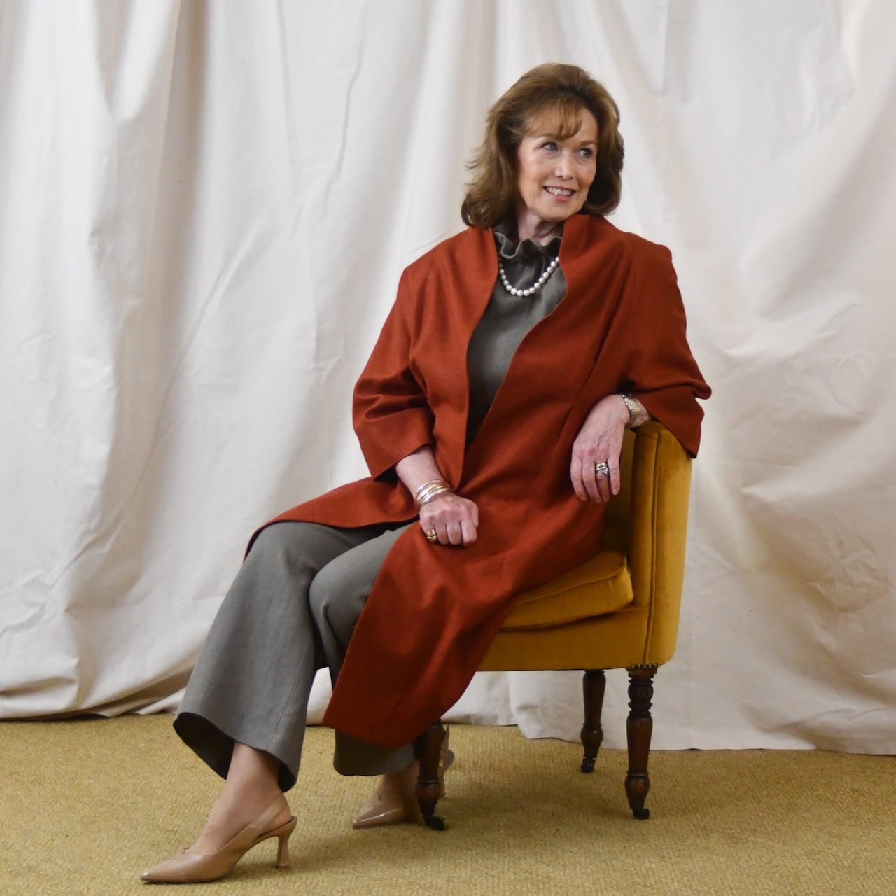 Summer Weight Cocoon Coat in Terracotta Silk. A Bespoke Silk Matka Cocoon Shaped Coat with under-bust and rear gathers, creating a shapely silhoutte.
Handmade in Britain. Seated View.