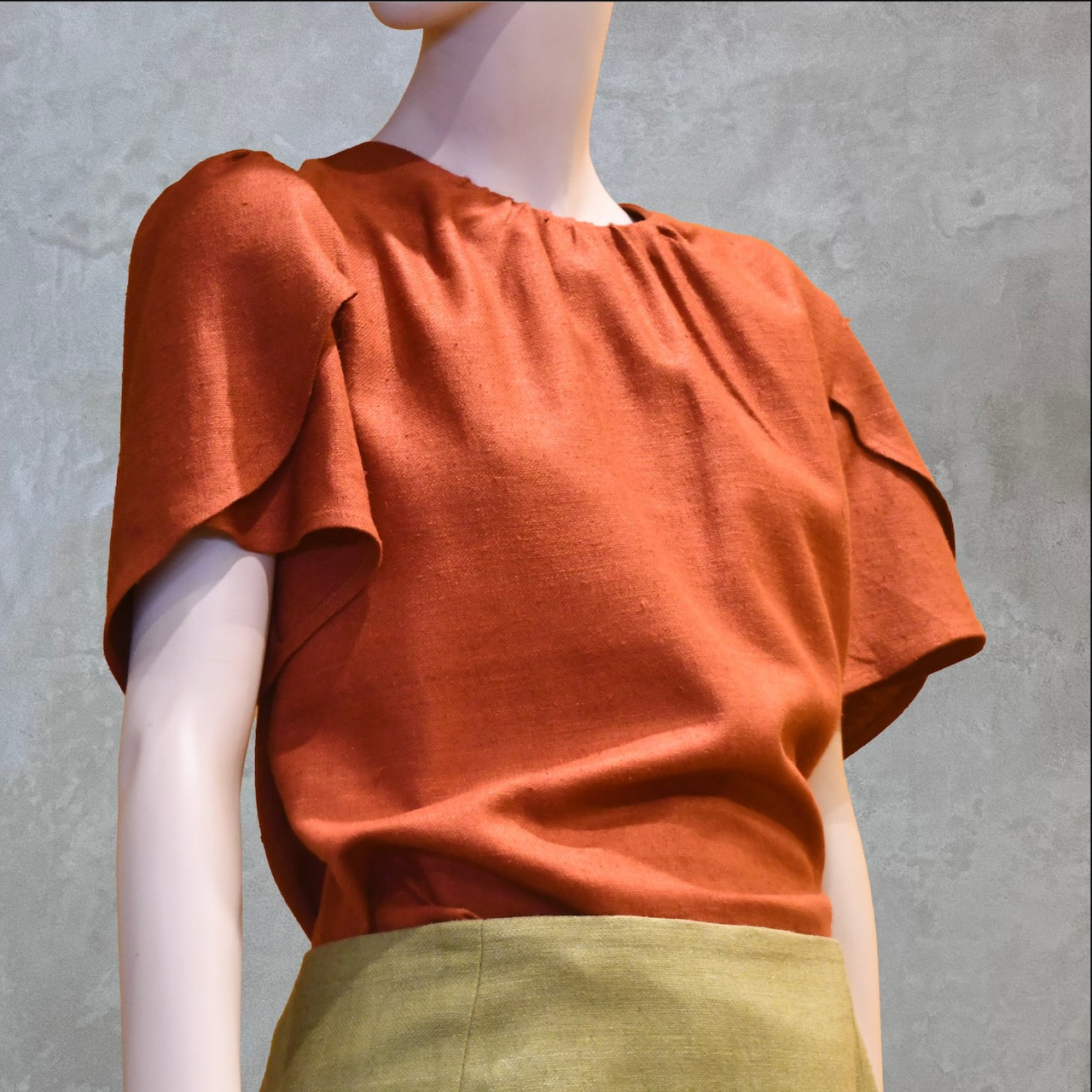 A Tulip Sleeve Blouse in Burnt Brick Silk Matka paired with an olive-green skirt. Handmade in Britain.