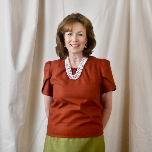 A Tulip Sleeve Blouse in Burnt Brick Silk Matka paired with an olive-green skirt. Handmade in Britain.