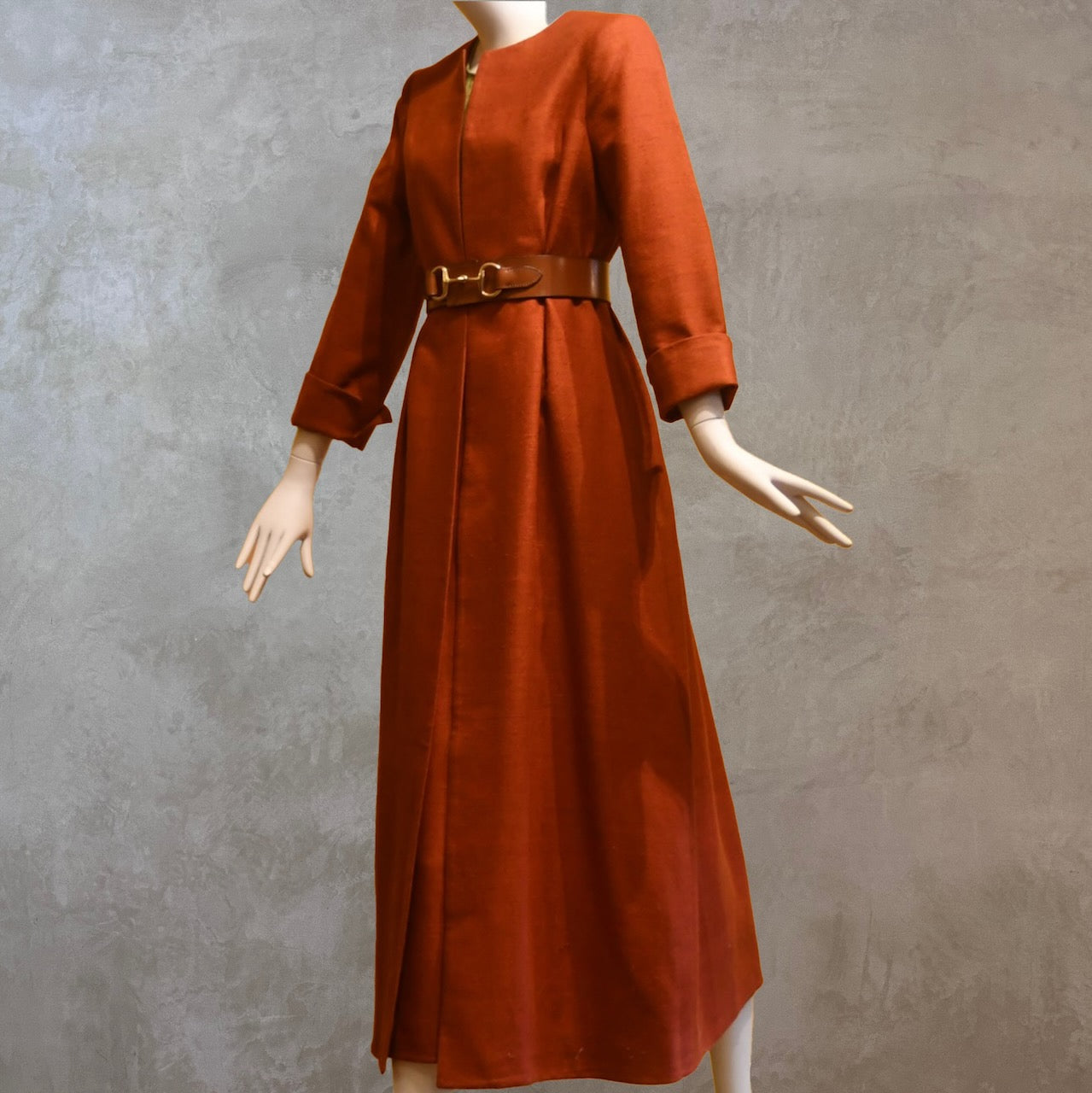 Tailored, Fitted Hourglass shaped coat in a summer-weight Silk in a terracotta colour. This is a three-quarter-sleeved, calf-length blue summer coat with an hourglass and skirted shape. Shown from the side-front, belted. A perfect summer coat for weddings and special occasions. Handmade in Britain.