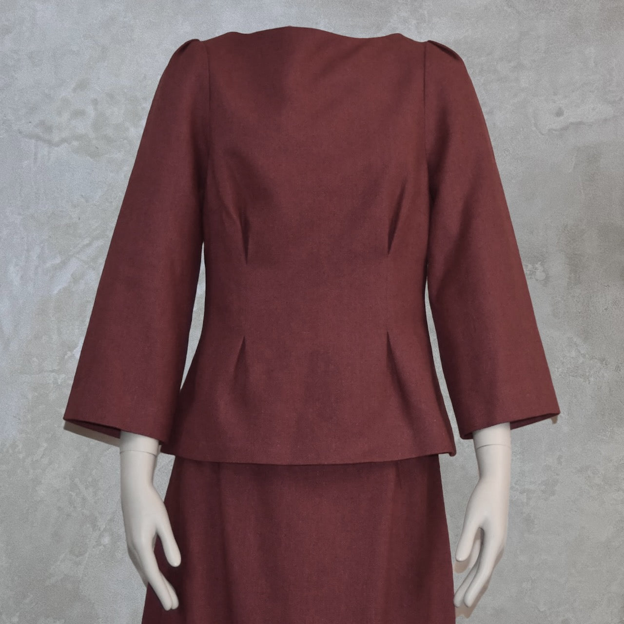 A close up view of a Tailored Boat Neck Skirt Suit in Damson Silk Matka, featuring a fitted long-sleeve top and matching skirt. Handmade in Britain.