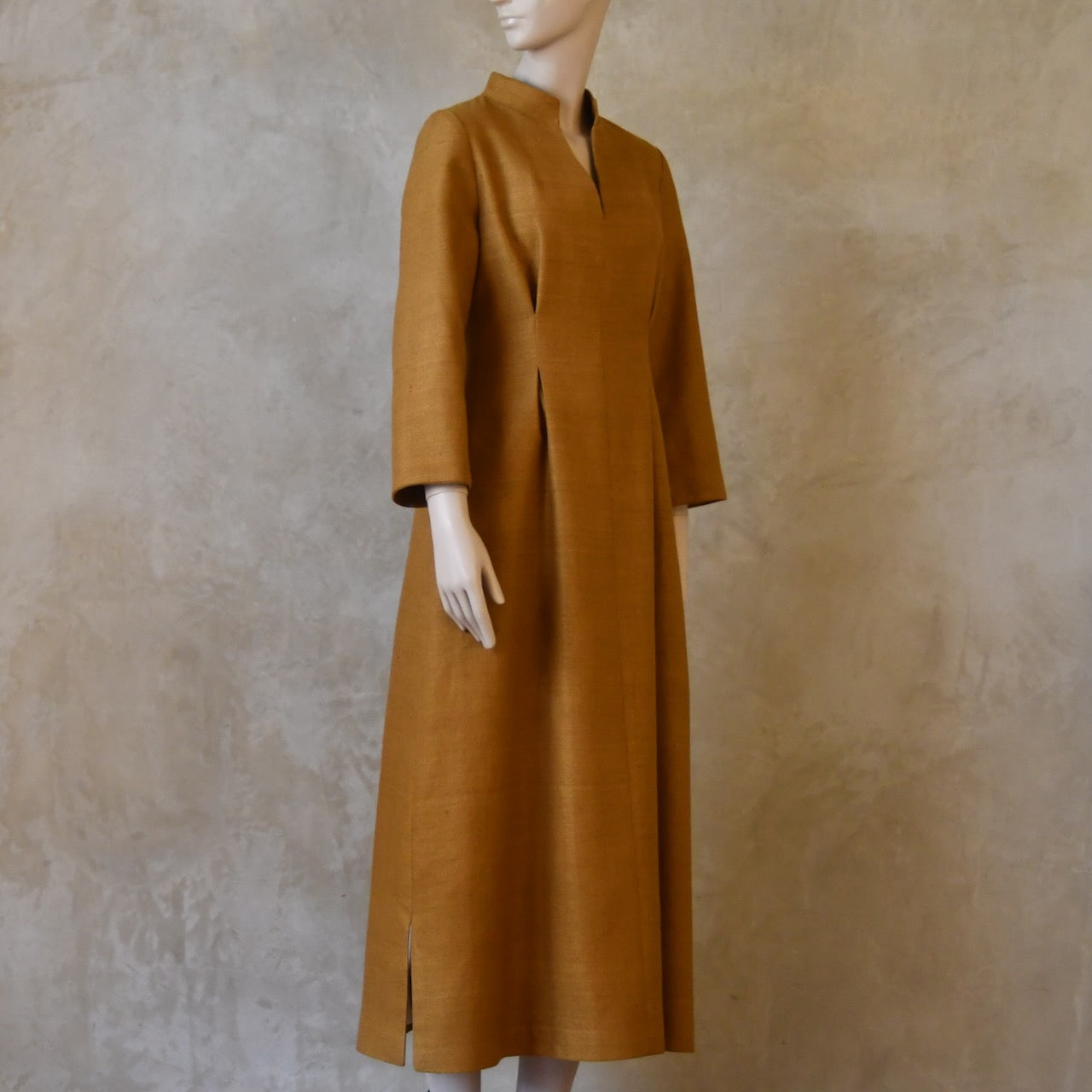 Angled shot of Tan coloured tailored formal wear silk dress. Three quarter length sleeves, fully lined in silk with gathering darts at front and rear creating flattering hourglass shape. Handmade in London.