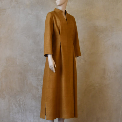 Angled shot of Tan coloured tailored formal wear silk dress. Three quarter length sleeves, fully lined in silk with gathering darts at front and rear creating flattering hourglass shape. Handmade in London.