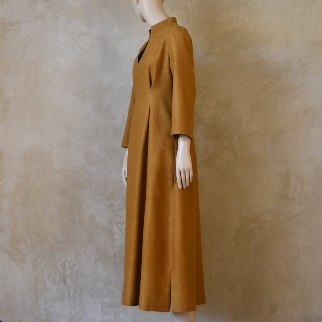 Turning side shot of Tan coloured tailored formal wear silk dress. Three quarter length sleeves, fully lined in silk with gathering darts at front and rear creating flattering hourglass shape. Handmade in London.