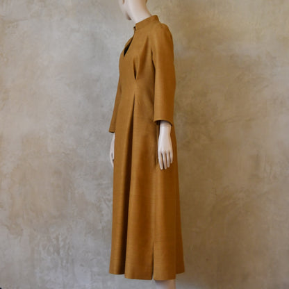 Turning side shot of Tan coloured tailored formal wear silk dress. Three quarter length sleeves, fully lined in silk with gathering darts at front and rear creating flattering hourglass shape. Handmade in London.