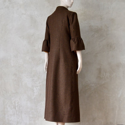 Angled back view of Bespoke Houndstooth patterned Merino Flannel Coat by EdNerat. Handmade in London, this A-Line longer length coat has gathered details at the shoulders, bell sleeves and is lined in pure silk. Woven in Somerset  by Fox Brothers and Handmade in London. 