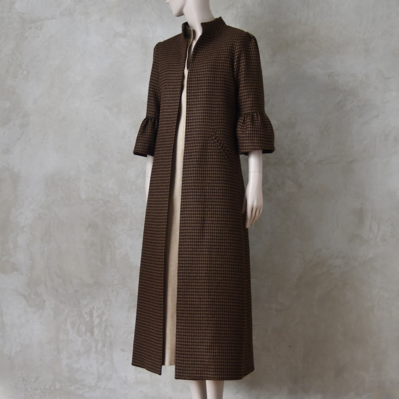 Bespoke Houndstooth patterned Merino Flannel Coat by EdNerat. Handmade in London, this A-Line longer length coat has gathered details at the shoulders, bell sleeves and is lined in pure silk. Woven in Somerset  by Fox Brothers and Handmade in London. Shown over Pale Silk Waisted Dress.