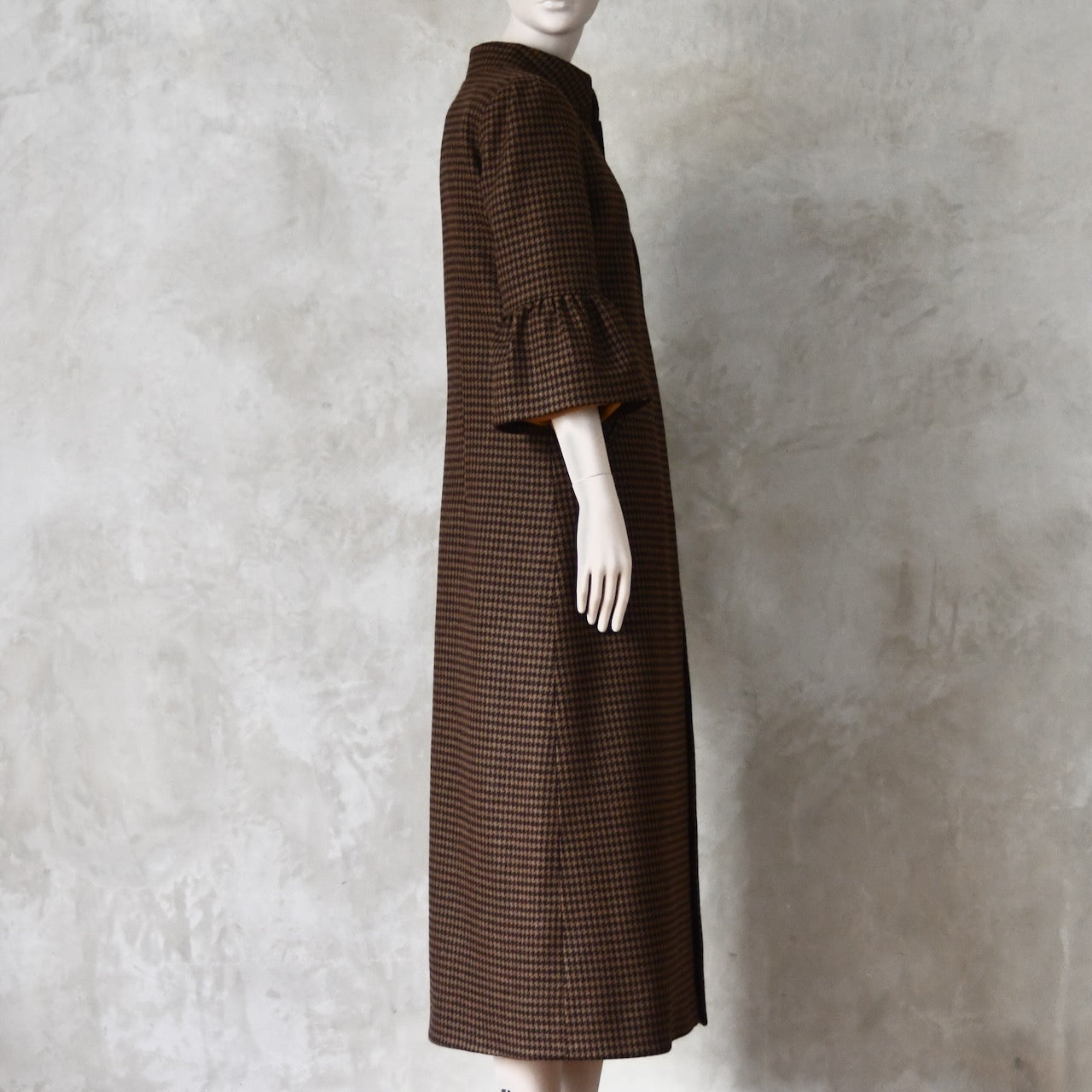 Side view of Bespoke Houndstooth patterned Merino Flannel Coat by EdNerat. Handmade in London, this A-Line longer length coat has gathered details at the shoulders, bell sleeves and is lined in pure silk. Woven in Somerset  by Fox Brothers and Handmade in London. 