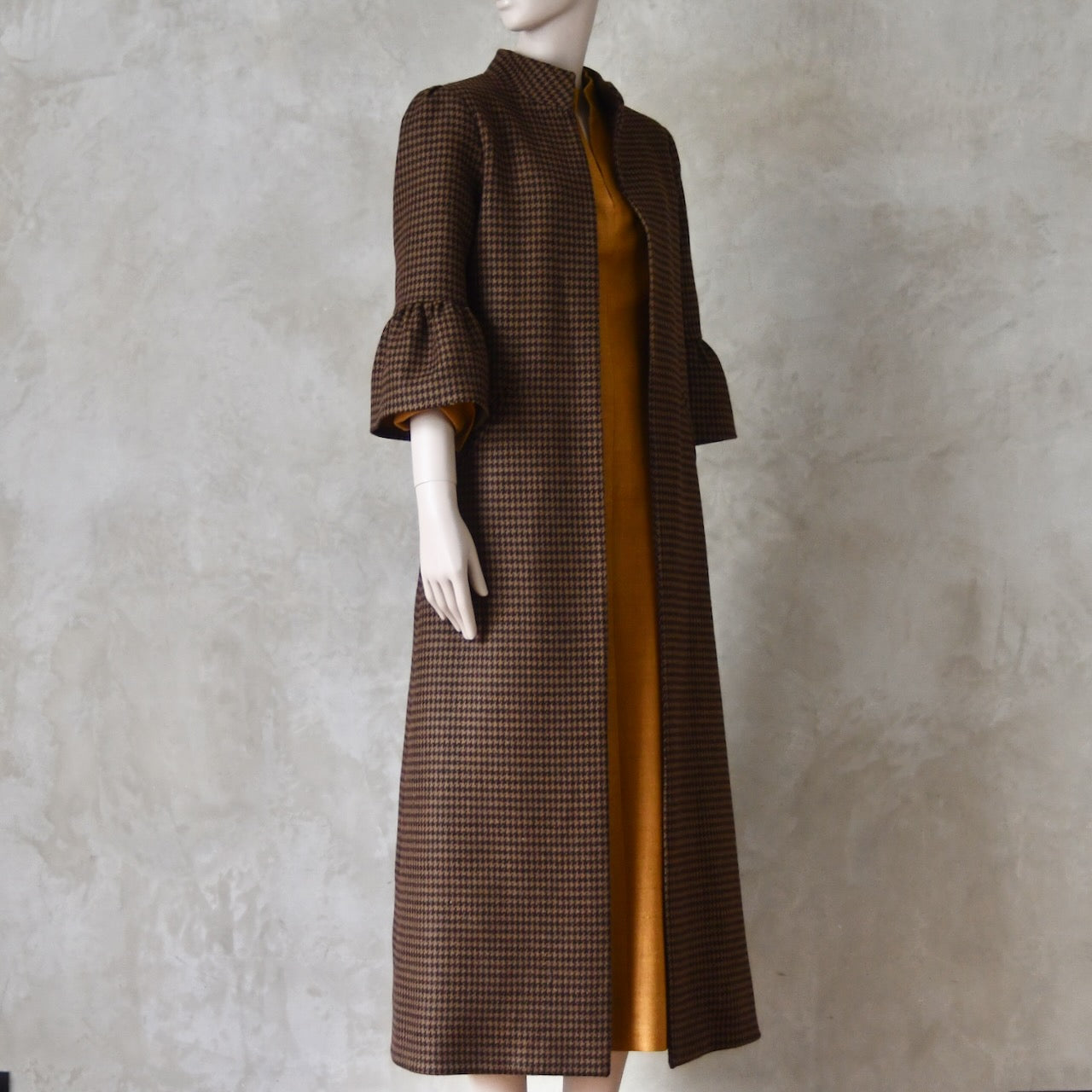 Bespoke Houndstooth patterned Merino Flannel Coat by EdNerat. Handmade in London, this A-Line longer length coat has gathered details at the shoulders, bell sleeves and is lined in pure silk. Woven in Somerset  by Fox Brothers and Handmade in London. Side View over Silk Waisted Dress.