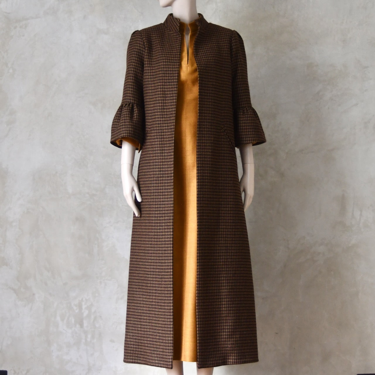 Bespoke Houndstooth patterned Merino Flannel Coat by EdNerat. Handmade in London, this A-Line longer length coat has gathered details at the shoulders, bell sleeves and is lined in pure silk. Woven in Somerset  by Fox Brothers and Handmade in London. Shown over Silk Waisted Dress.