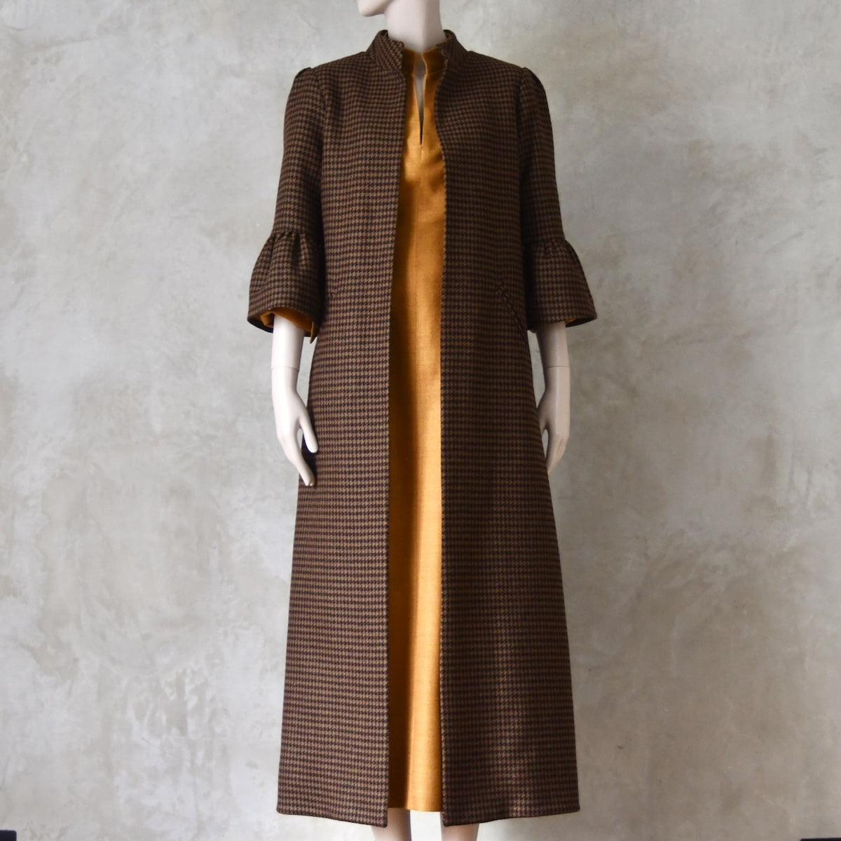 Bespoke Houndstooth patterned Merino Flannel Coat by EdNerat. Handmade in London, this A-Line longer length coat has gathered details at the shoulders, bell sleeves and is lined in pure silk. Woven in Somerset  by Fox Brothers and Handmade in London. Shown over Silk Waisted Dress.