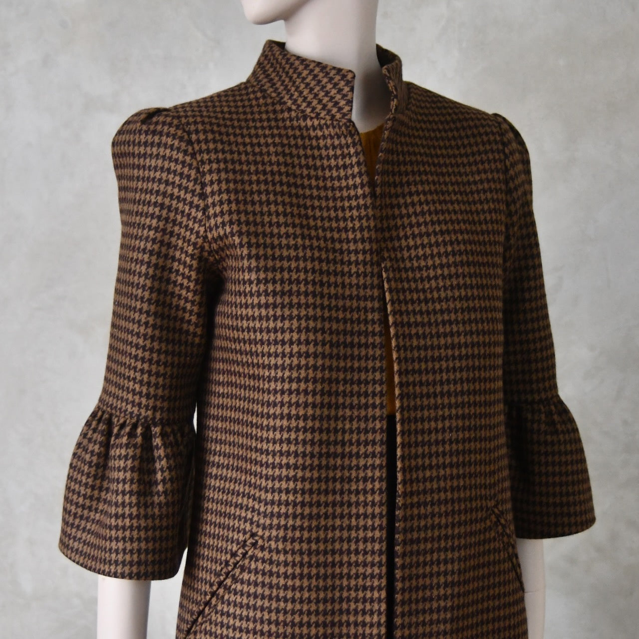 Close up of Bespoke Houndstooth patterned Merino Flannel Coat by EdNerat. Handmade in London, this A-Line longer length coat has gathered details at the shoulders, bell sleeves and is lined in pure silk. Woven in Somerset  by Fox Brothers and Handmade in London. 