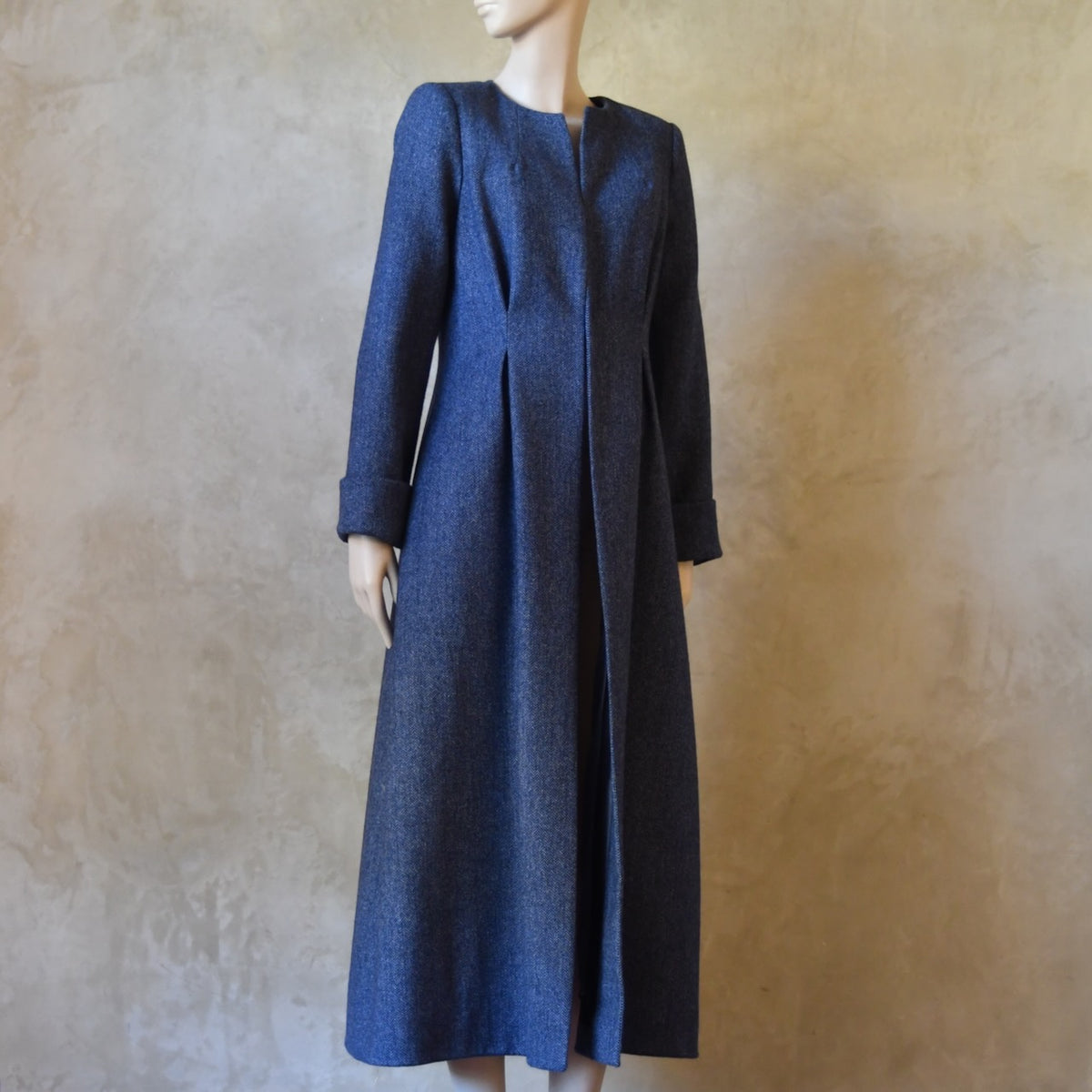 Side view of Bespoke Waisted Tweed Coat, Handmade in London. Denim Blue herringbone tweed dress coat, ideal for winter weddings, race fixtures and other formalwear occasions. Fully lined in pure silk, with optional Nehru collar, fold back cuffs and self-fabric wrap around belt.
Longer or calf length coat.