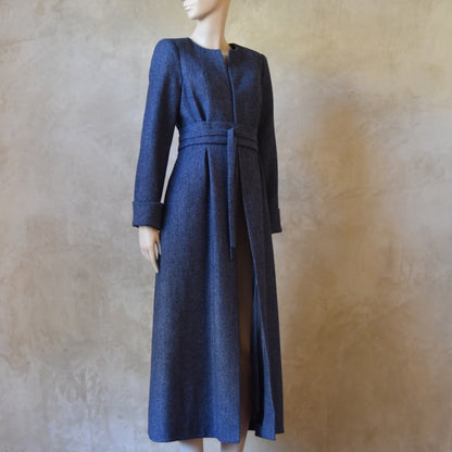 Side Angled view of Bespoke Belted Blue Tweed Coat, Handmade in London. Denim Blue herringbone tweed dress coat, ideal for winter weddings, race fixtures and other formalwear occasions. Fully lined in pure silk, with optional Nehru collar, fold back cuffs and self-fabric wrap around belt.
Longer or calf length coat.