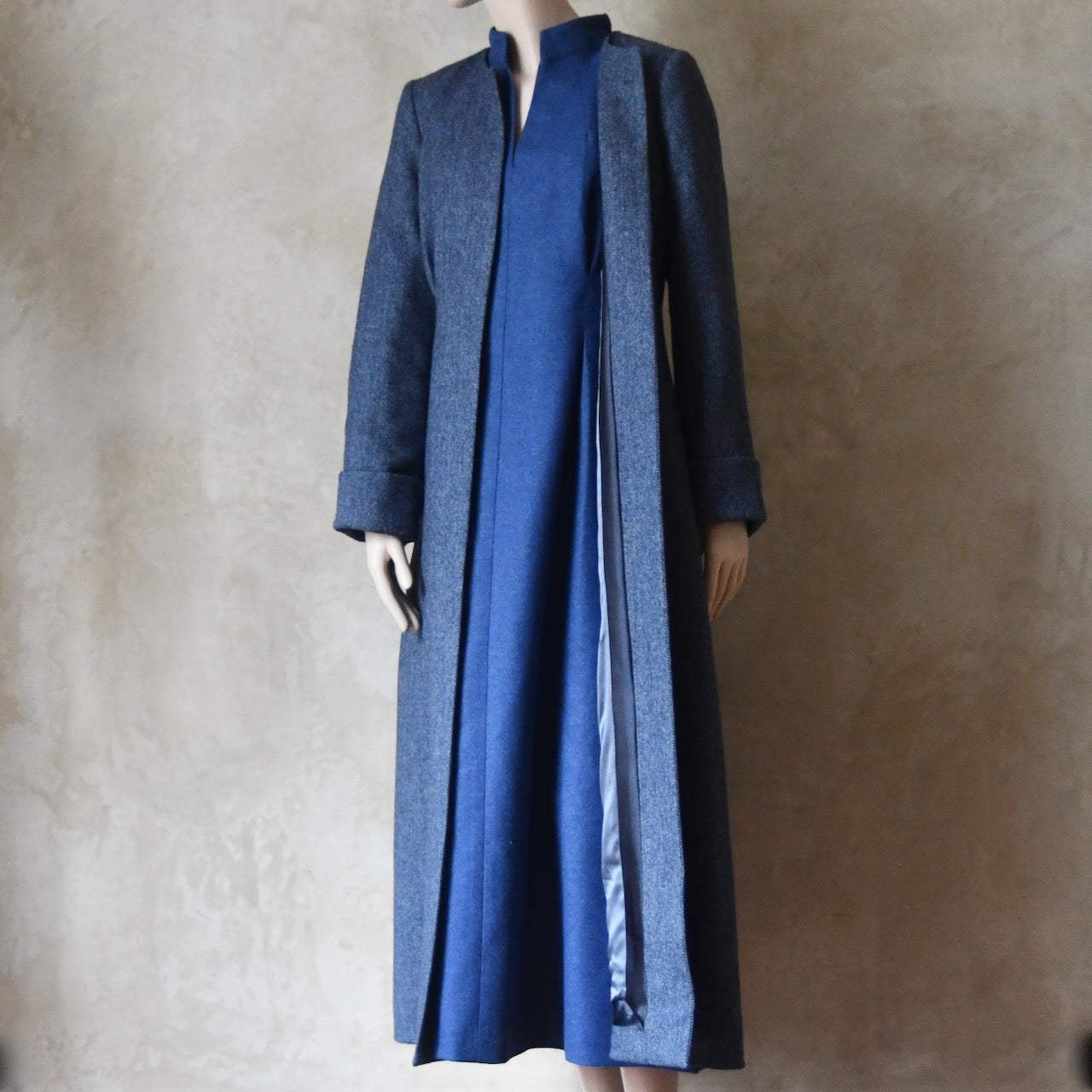 Bespoke Hourglass Tweed Coat, worn over Formal Merino Flannel Dress. Handmade in London. Denim Blue herringbone tweed dress coat, ideal for winter weddings, race fixtures and other formalwear occasions. Fully lined in pure silk, with optional Nehru collar, fold back cuffs and self-fabric wrap around belt.
Longer or calf length.