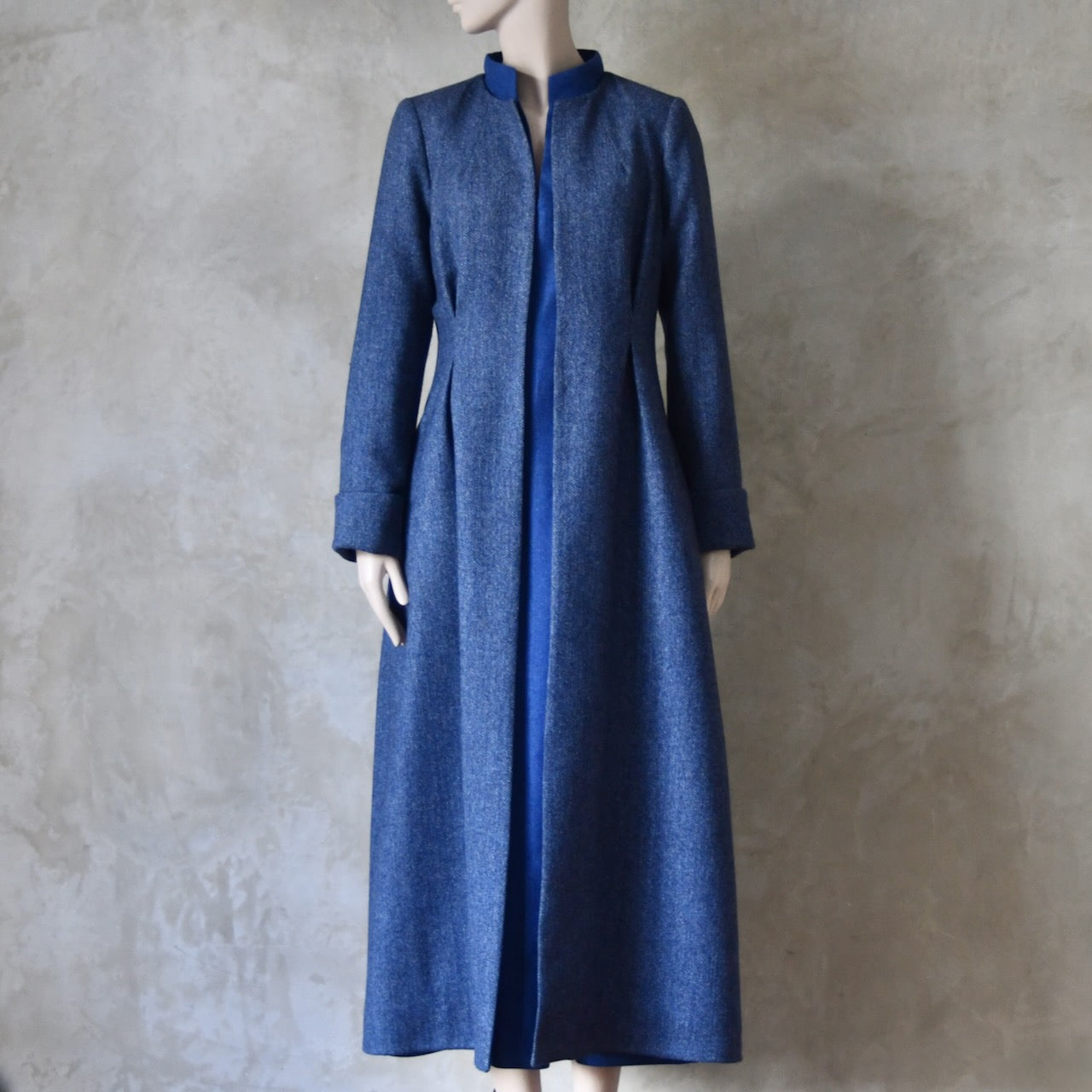 Bespoke Hourglass Tweed Coat, worn over Waisted Merino Flannel Dress. Handmade in London. Denim Blue herringbone tweed dress coat, ideal for winter weddings, race fixtures and other formalwear occasions. Fully lined in pure silk, with optional Nehru collar, fold back cuffs and self-fabric wrap around belt.
Longer or calf length.