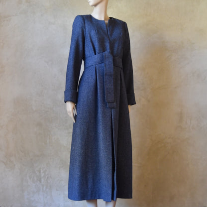 Side Angled view of Bespoke Hourglass Tweed Coat, Handmade in London. Denim Blue herringbone tweed dress coat, ideal for winter weddings, race fixtures and other formalwear occasions. Fully lined in pure silk, with optional Nehru collar, fold back cuffs and self-fabric wrap around belt.
Longer or calf length coat.