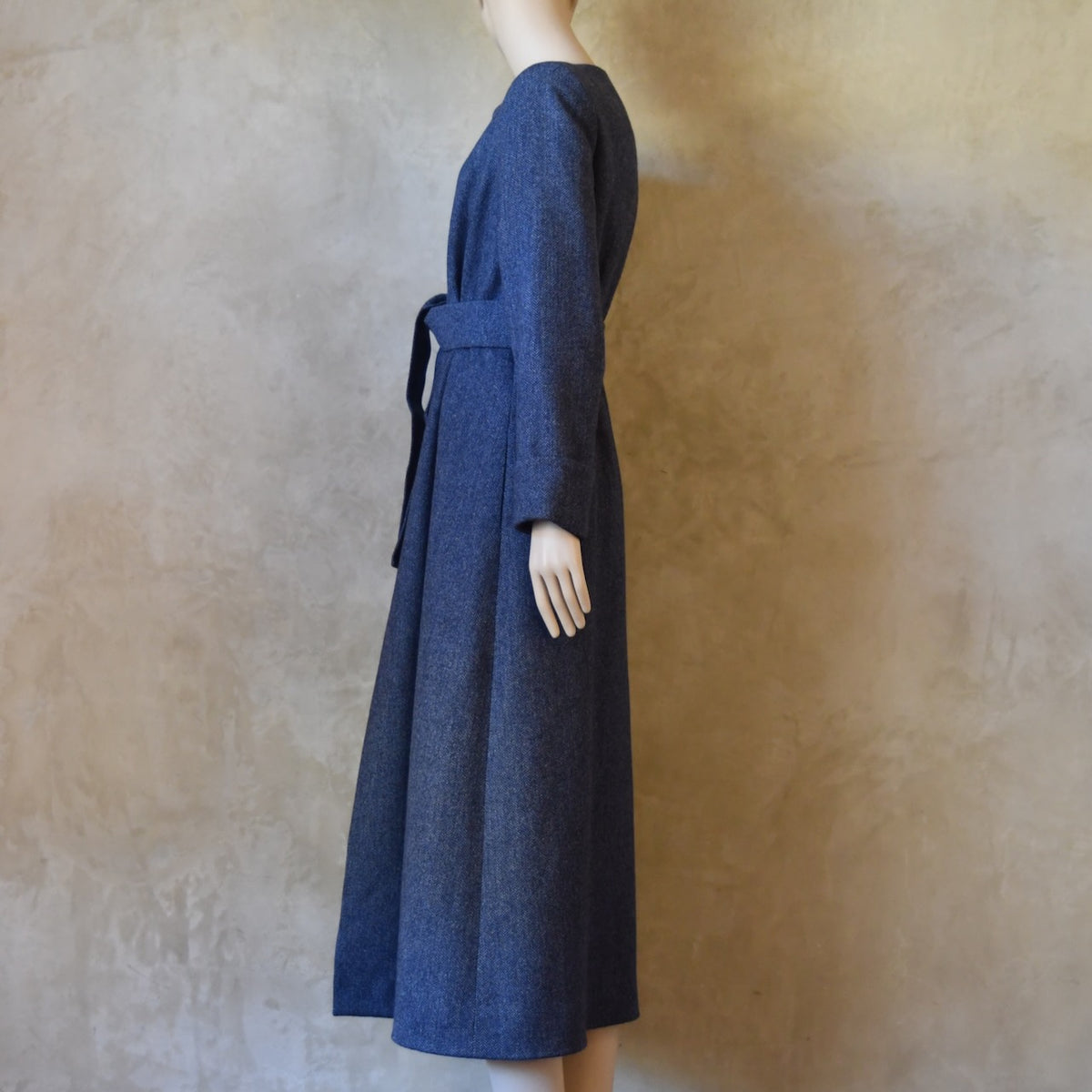 Side View of Bespoke Hourglass Tweed Coat, Handmade in London. Denim Blue herringbone tweed dress coat, ideal for winter weddings, race fixtures and other formalwear occasions. Fully lined in pure silk, with optional Nehru collar, fold back cuffs and self-fabric wrap around belt.
Longer or calf length coat.