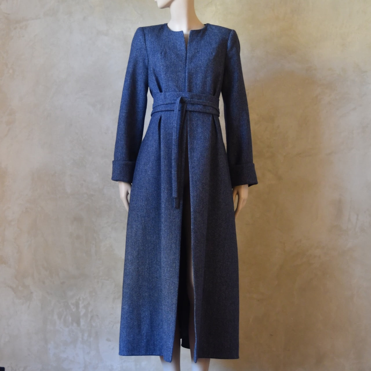 Bespoke Belted Blue Tweed Coat, Handmade in London. Denim Blue herringbone tweed dress coat, ideal for winter weddings, race fixtures and other formalwear occasions. Fully lined in pure silk, with optional Nehru collar, fold back cuffs and self-fabric wrap around belt.
Longer or calf length coat.