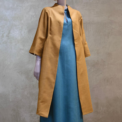 Full length shot of the EdNerat Silk Cocoon Coat in Tan, worn over the Skirted Hourglass Dress in Emerald Green. A mid length summer coat, perfect for throwing over the most relaxed of outfits. Handmade in London.