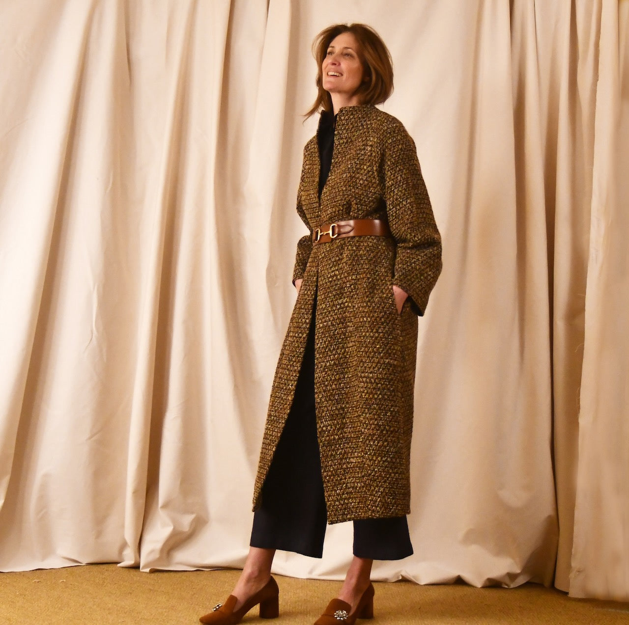 Long cocoon coat in Linton Tweeds Golden Brown, Black and Camel Boucle. Shown belted at the waist, this elegant coat falls tot he mid calf. Handmade in Britain.