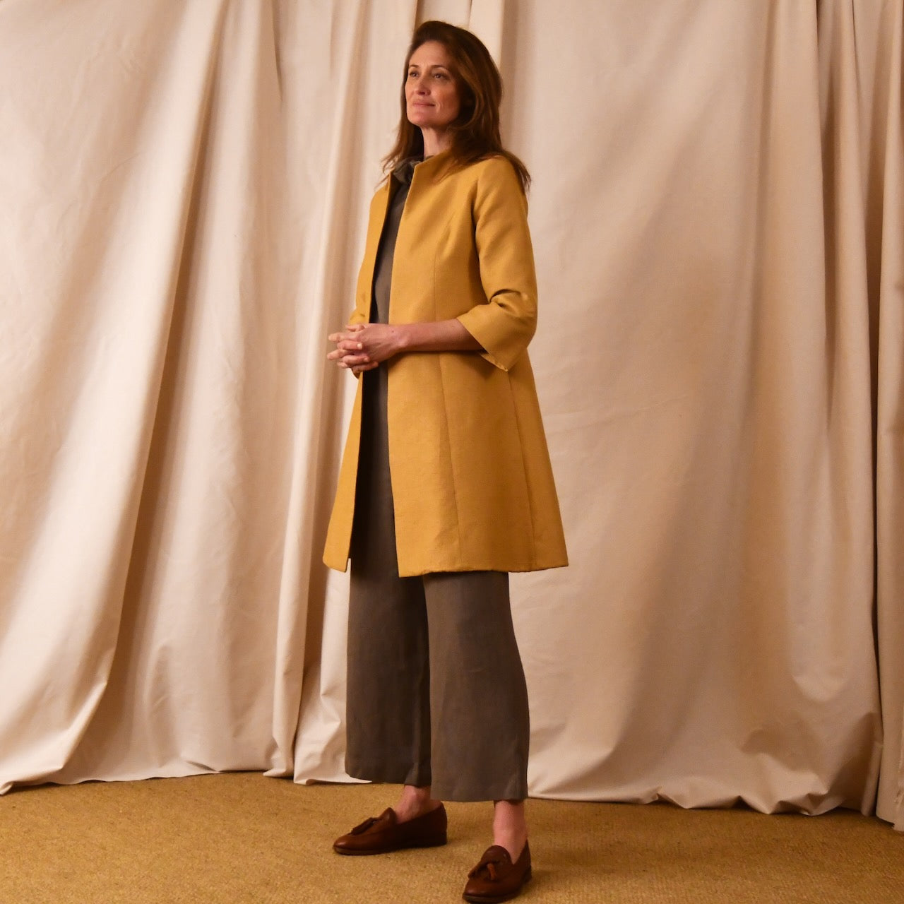 Bespoke Trapeze Swing Coat in Golden Yellow Brocade. Spring Summer MidLength Swing Coat with slight vintage feel and flattering seaming details to front and rear. Shown in side view over contrast linen pant suit.